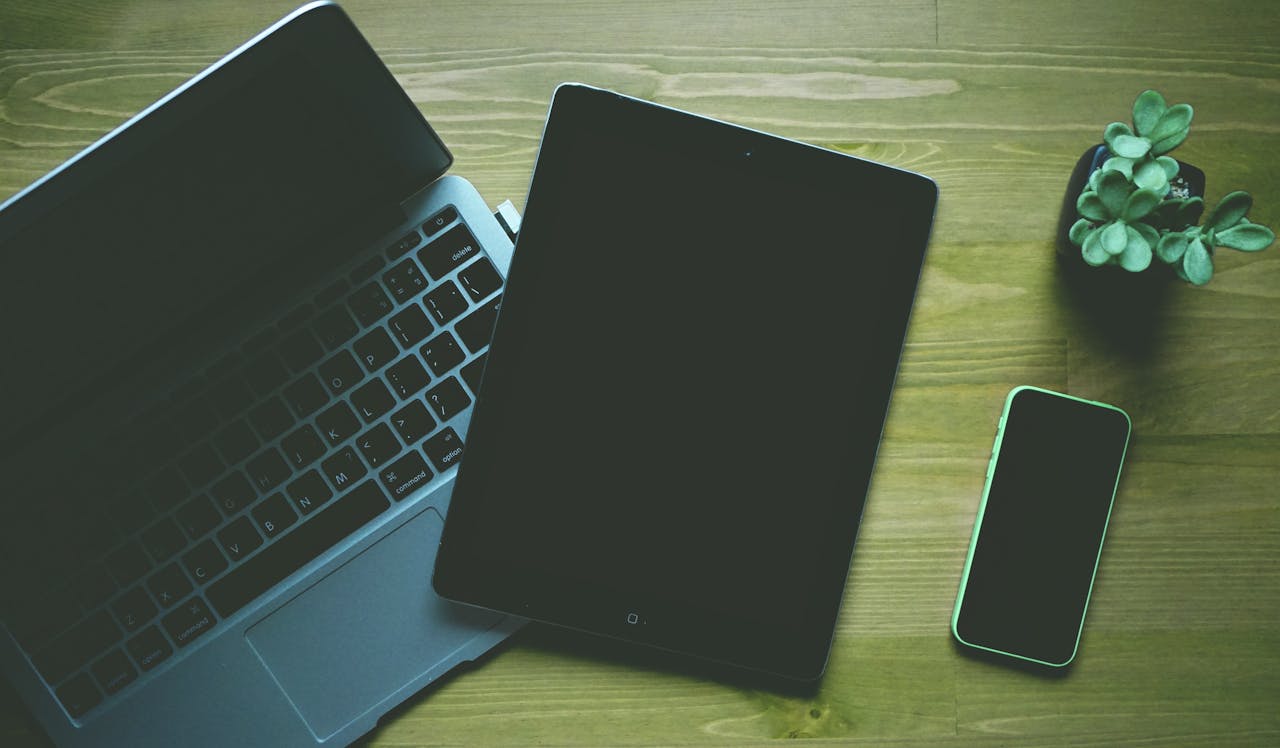 A top-down view of a workspace featuring a laptop, tablet, smartphone, and a small plant.