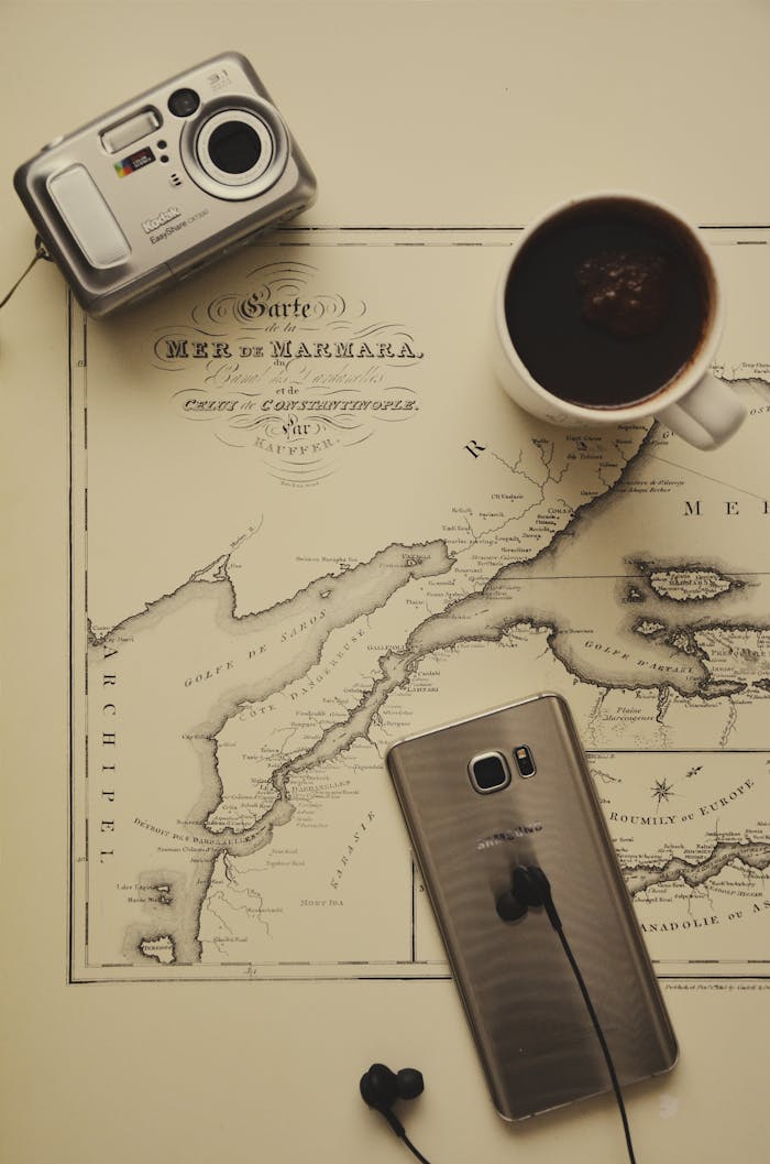 A flat lay of vintage map, coffee mug, camera, and smartphone. Ideal for travel and nostalgia themes.