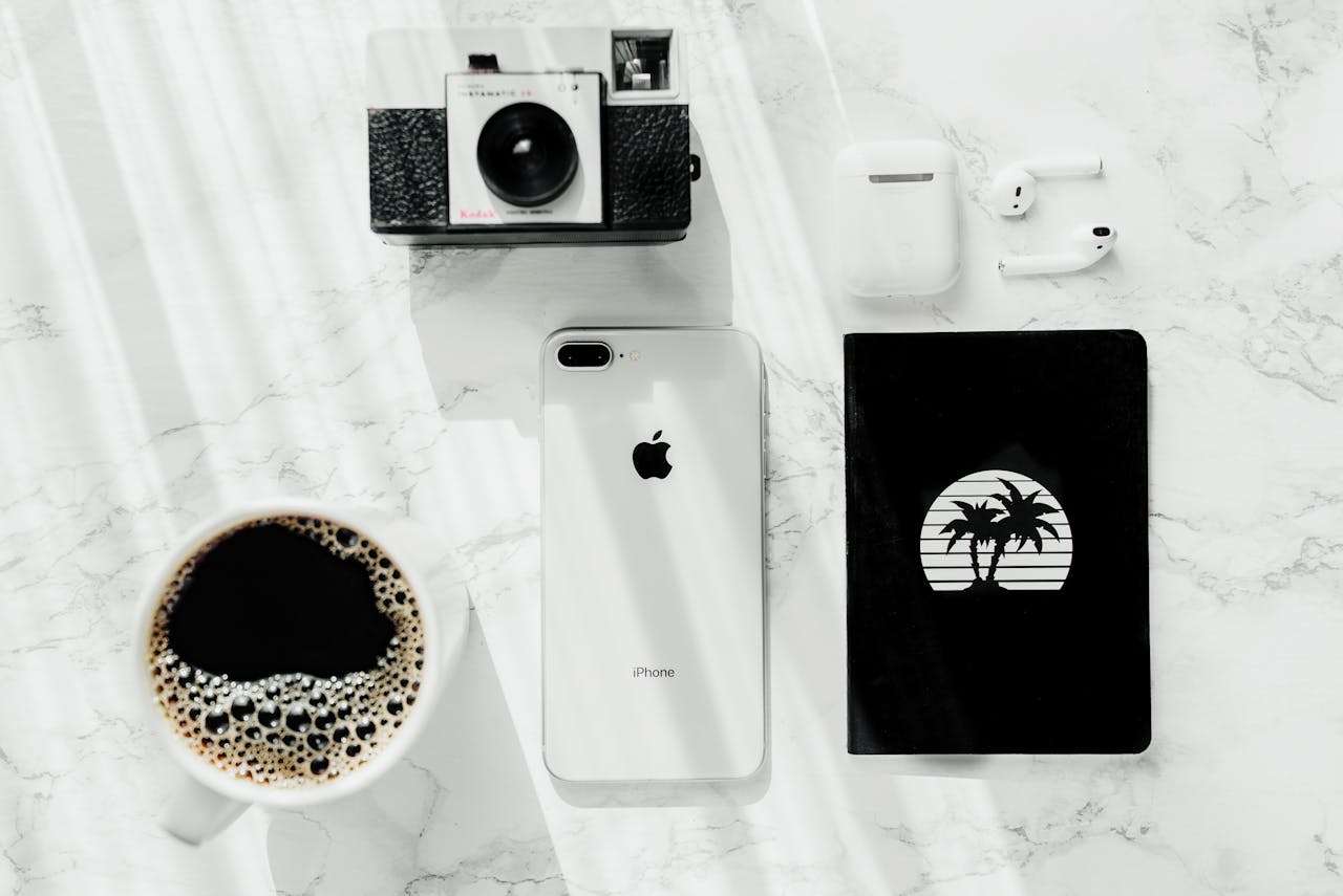 Stylish flat lay scene featuring a vintage camera, iPhone, AirPods, and coffee on a marble surface.